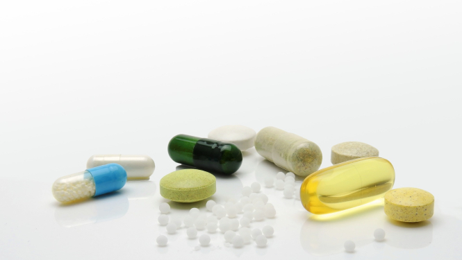 Uz galda izbērtas dažāda izmēra un krāsas zāļu kapsulas