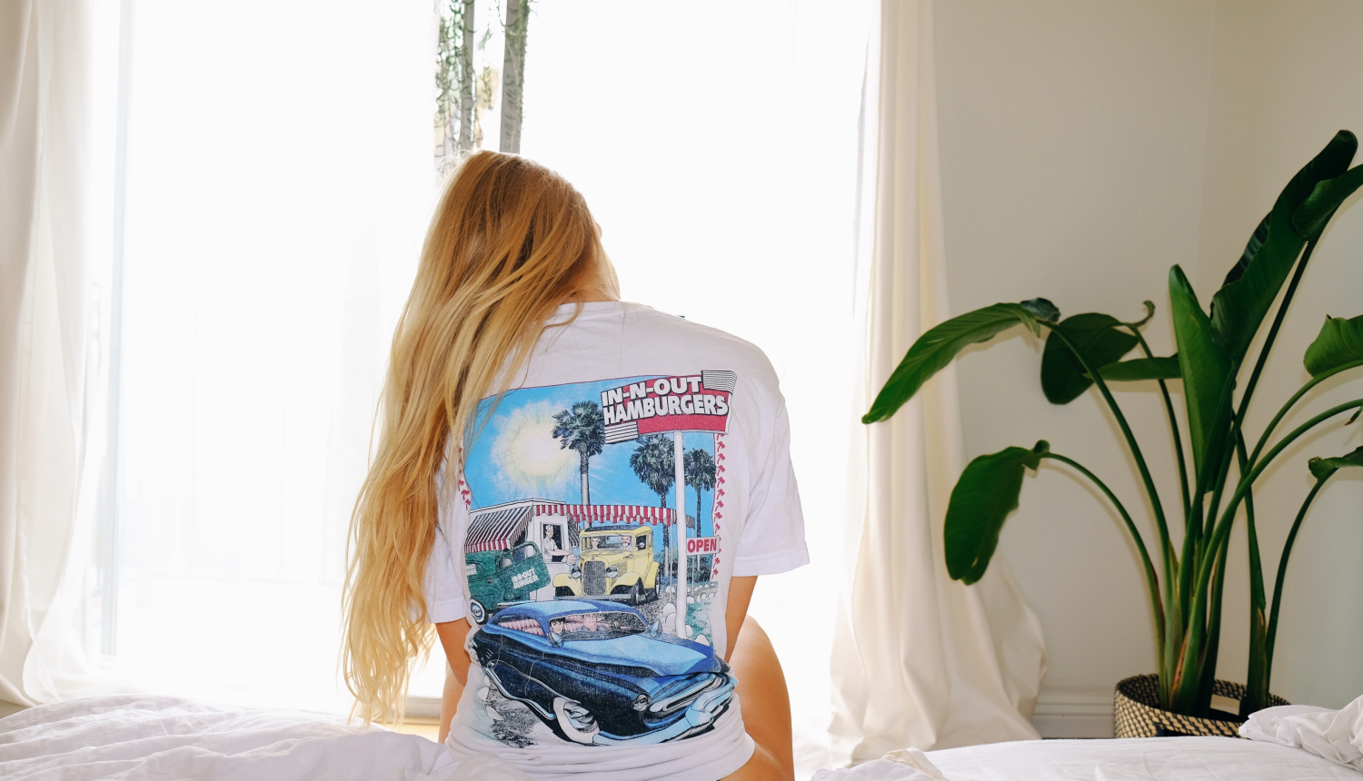 Foto: Meitene sēž uz gultas ar skatu uz logu