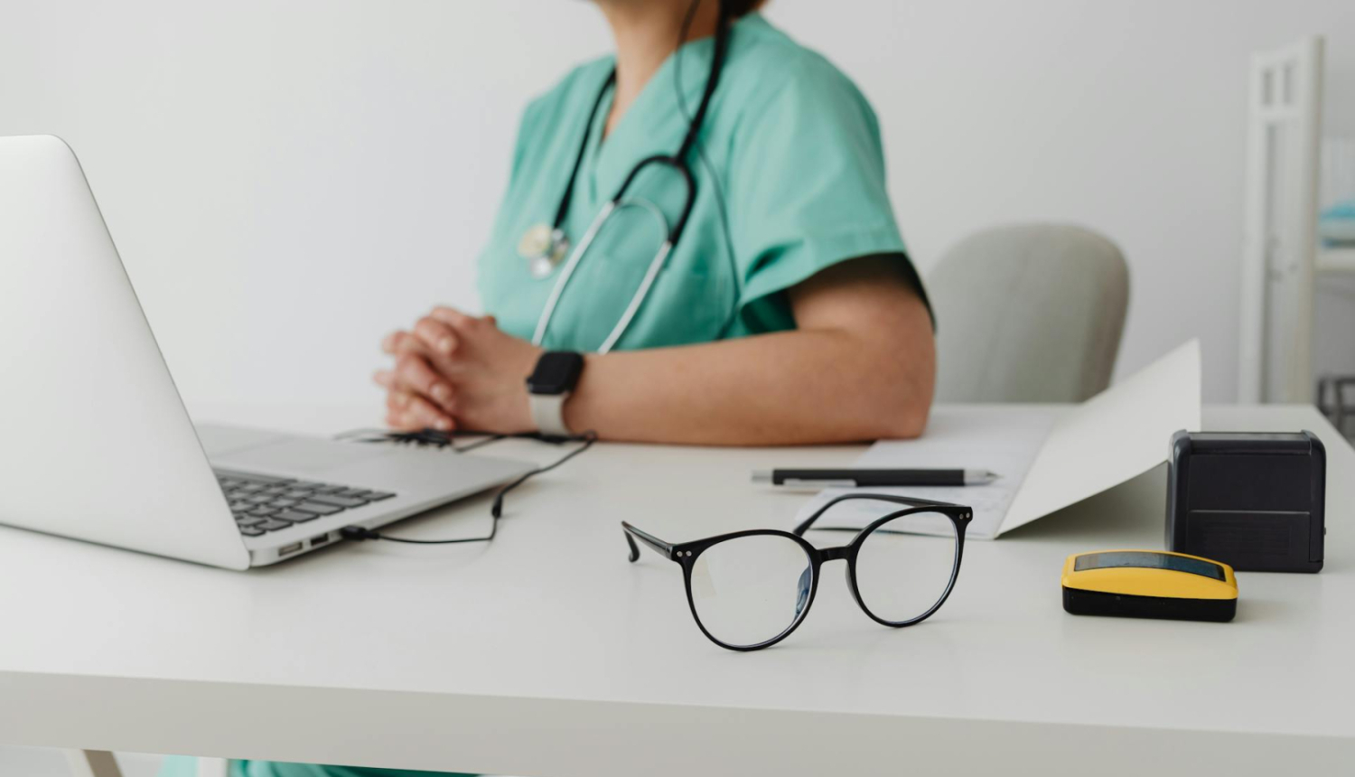 Ārsts sēž pie galda un skatās datorā