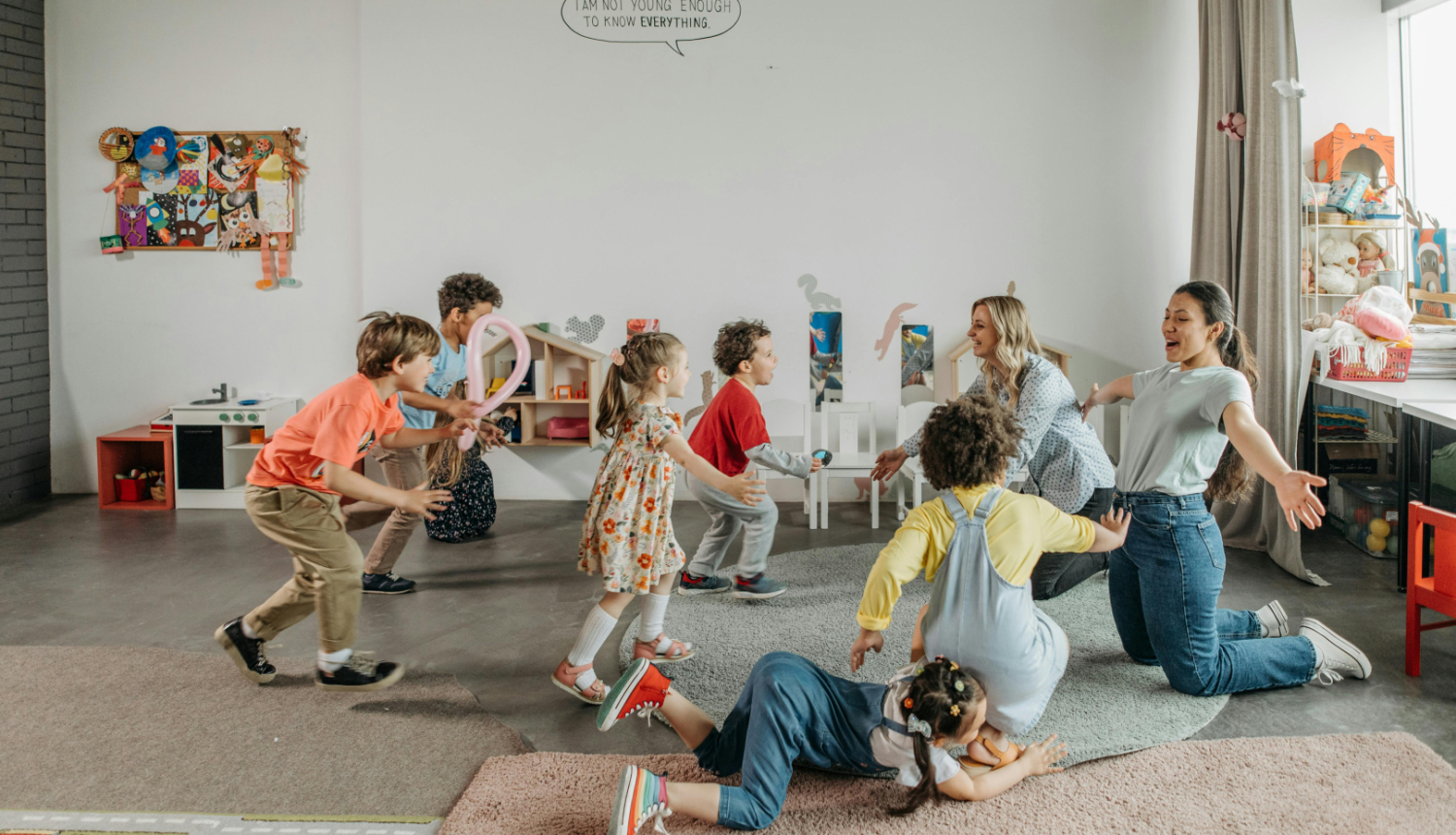 Priecīgi bērni rotaļājas kopā ar savām audzinātājām